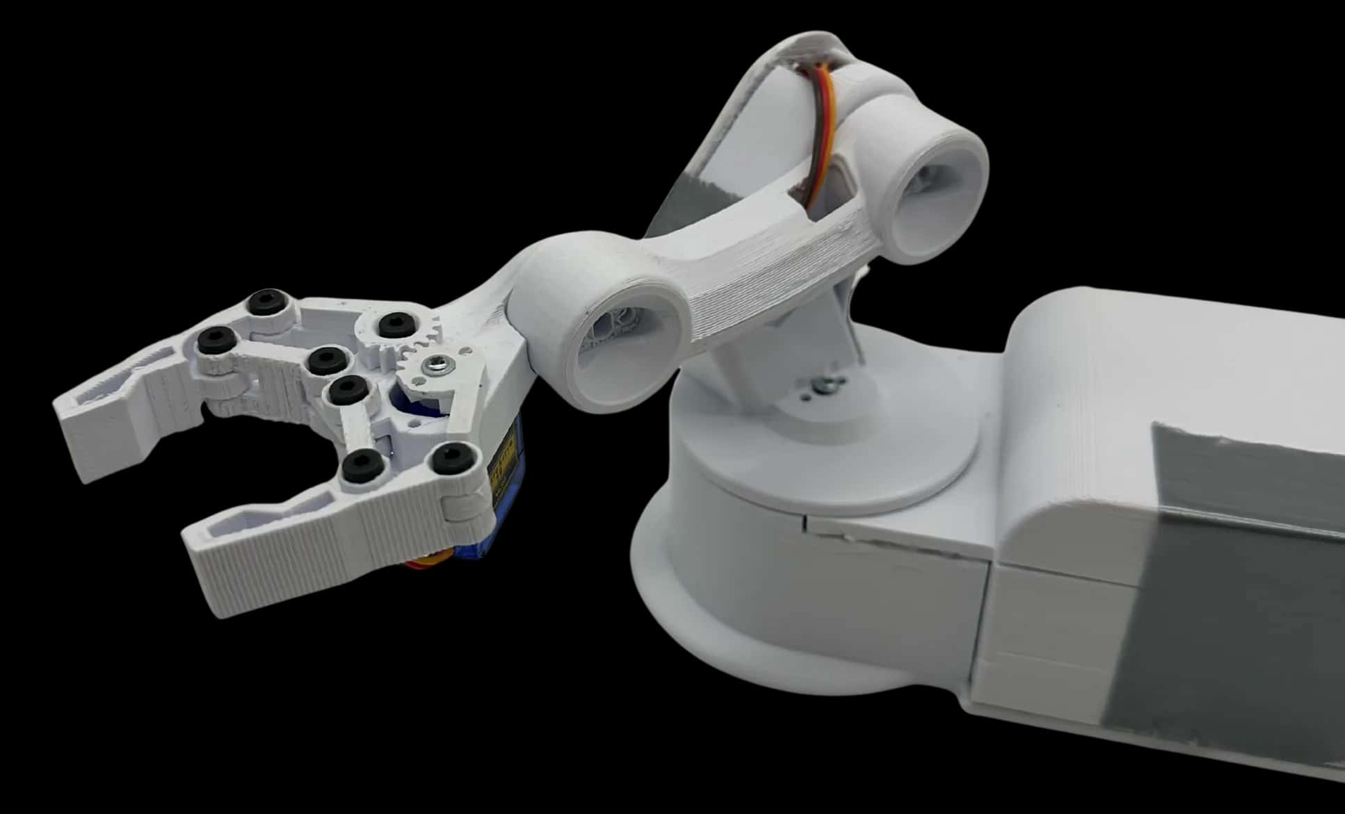 The finished robotic arm as a cut-out: a white PLA two-finger claw with black screw heads and a blue micro servo, a dog-bone forearm link with orange servo wires, and the turntable base running off the right edge
