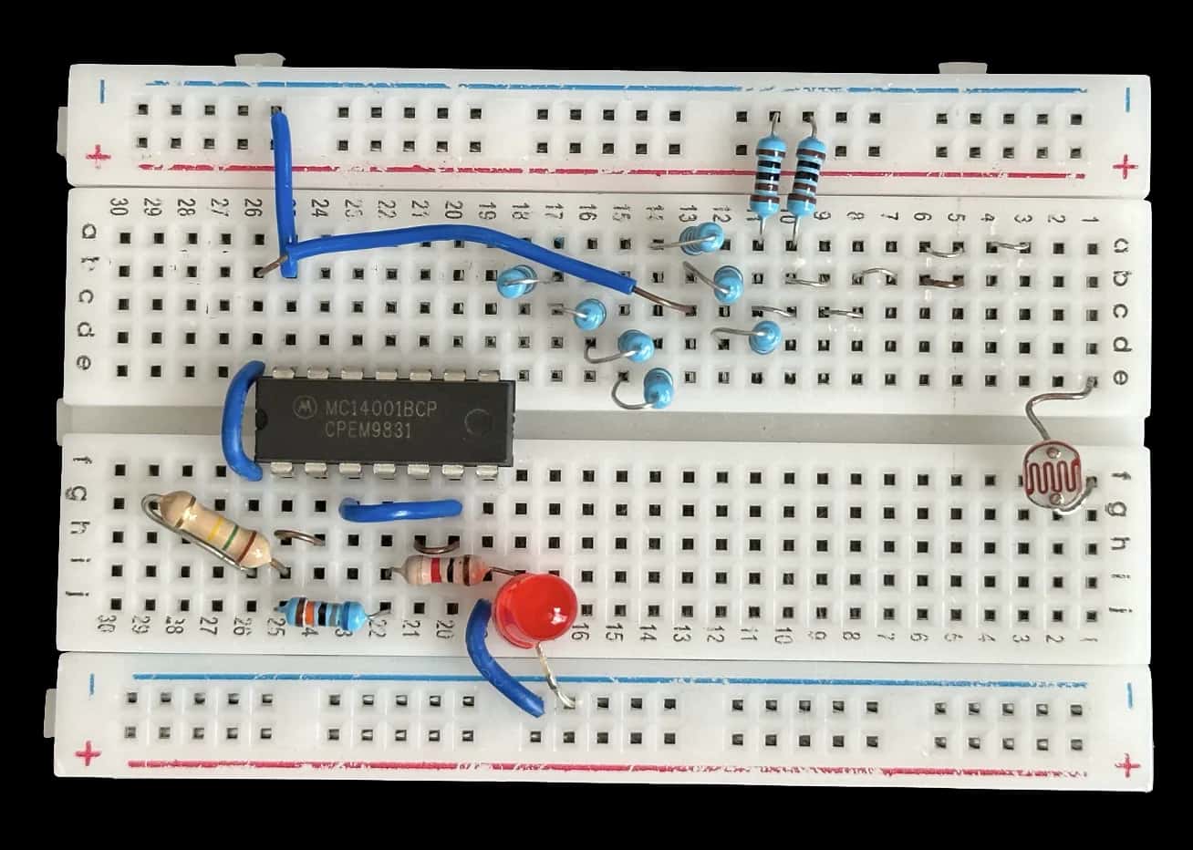 Top-down cut-out of the finished breadboard circuit: an MC14001BCP quad NOR-gate chip, blue and beige resistors, a red LED and a light-dependent resistor