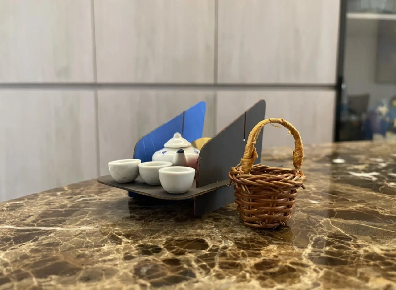 The scale model in table mode on a marble counter, laid with a miniature tea set beside a small wicker basket.