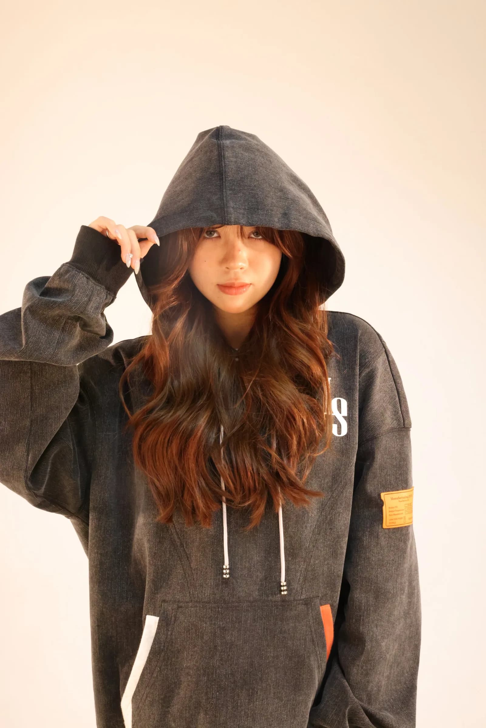 Model with long hair wearing the washed denim hoodie with the hood up and the orange label on the sleeve