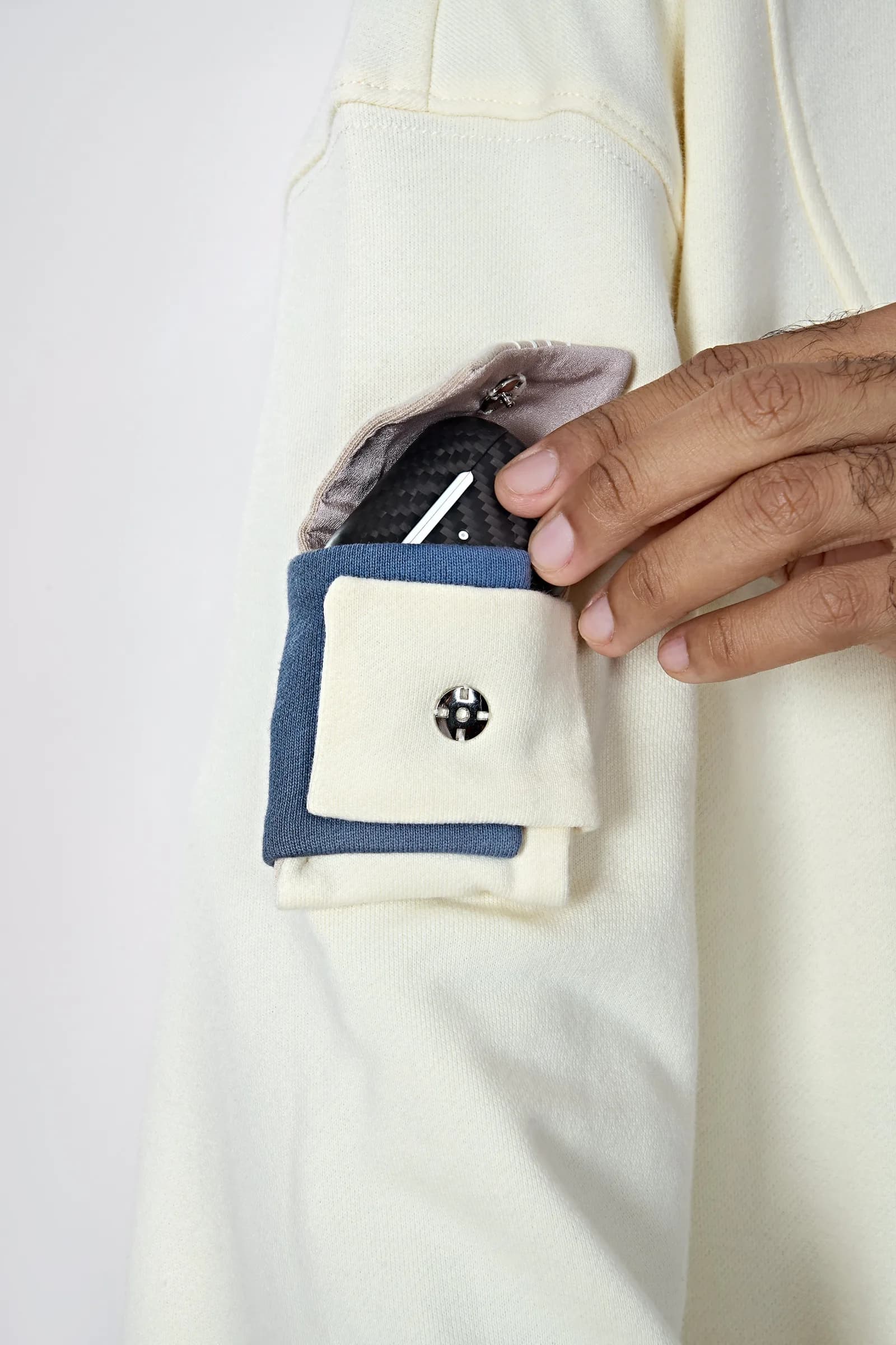 A hand pulling earbuds from the layered sleeve pocket of the Cream White Hoodie