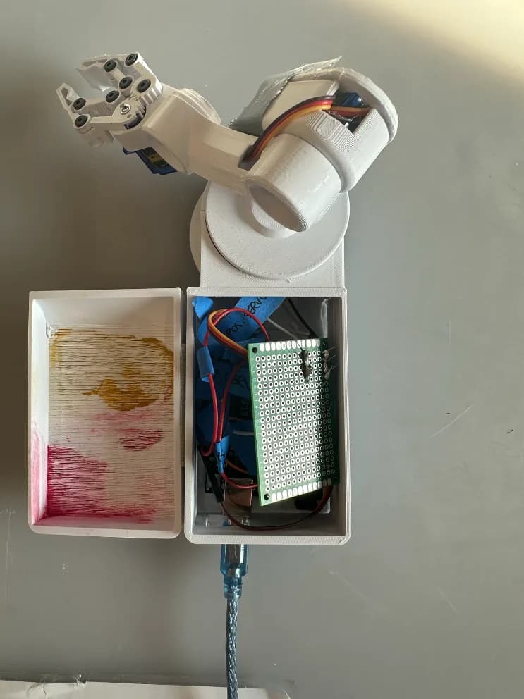 Top-down view of the arm with its base open: the protoboard mounted inside, the removable cap set beside it, a USB cable leaving the rear