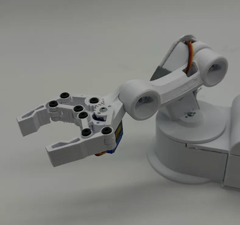 Close crop of the open claw and dog-bone forearm link above the turntable, orange servo wires running along the arm