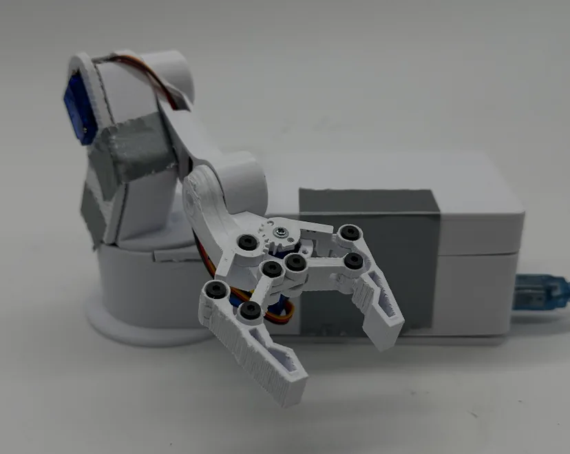 The finished arm with the claw angled down toward the camera in front of the base, a grey tape accent on the forearm