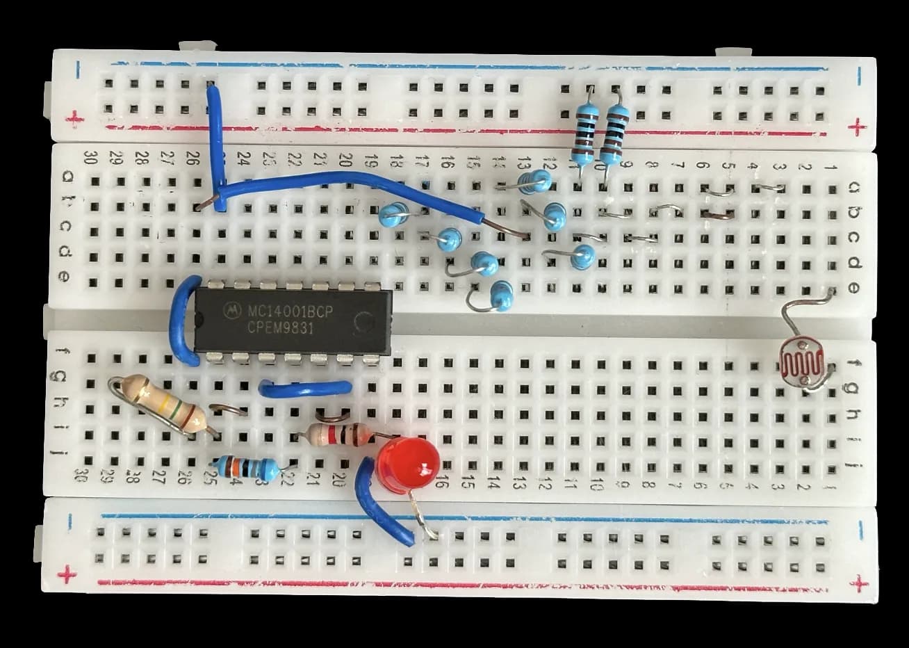 Top-down cut-out of the finished breadboard circuit: an MC14001BCP quad NOR-gate chip, blue and beige resistors, a red LED and a light-dependent resistor
