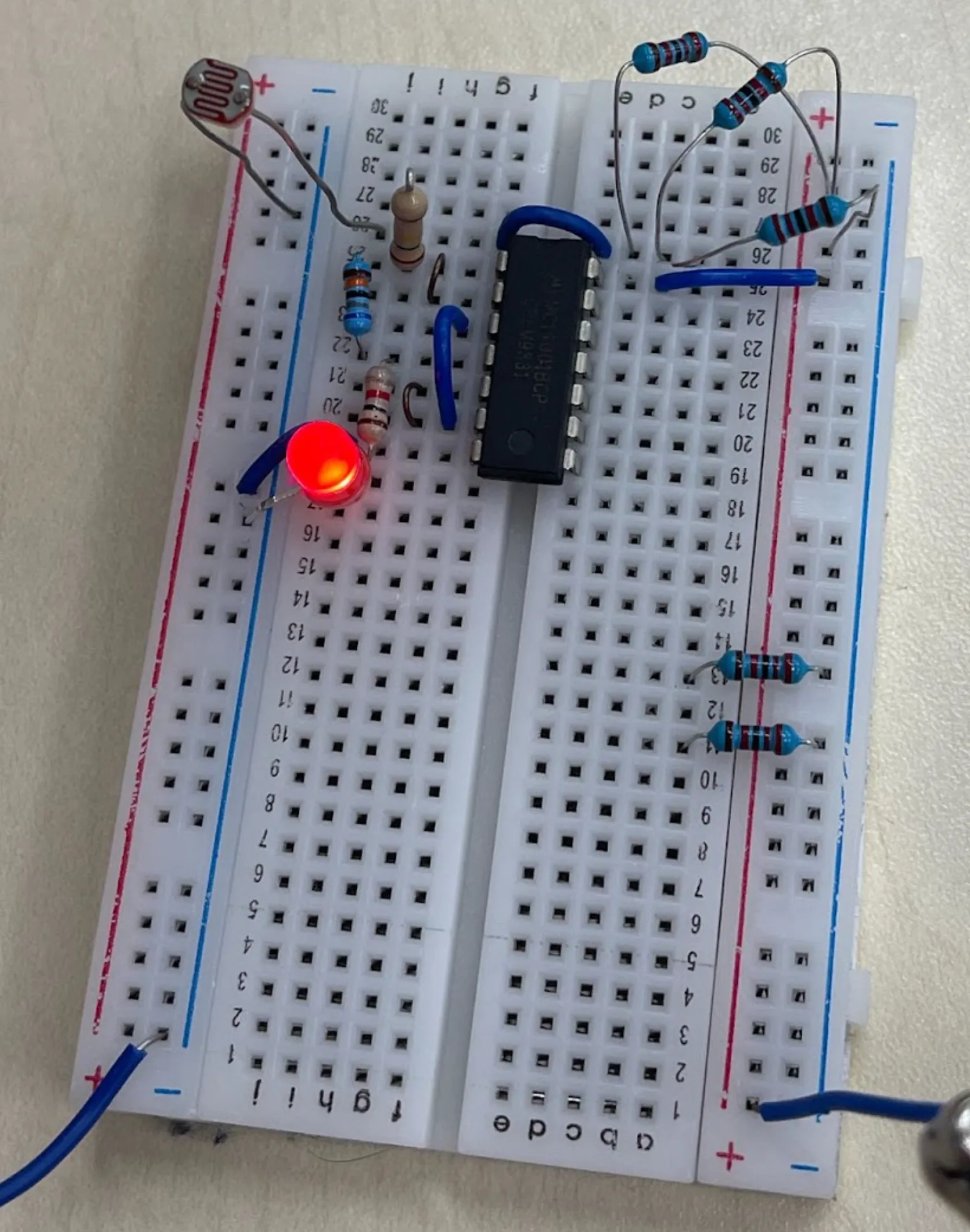 The breadboard circuit at an angle with its red LED lit, the light-dependent resistor bent over the top-left corner