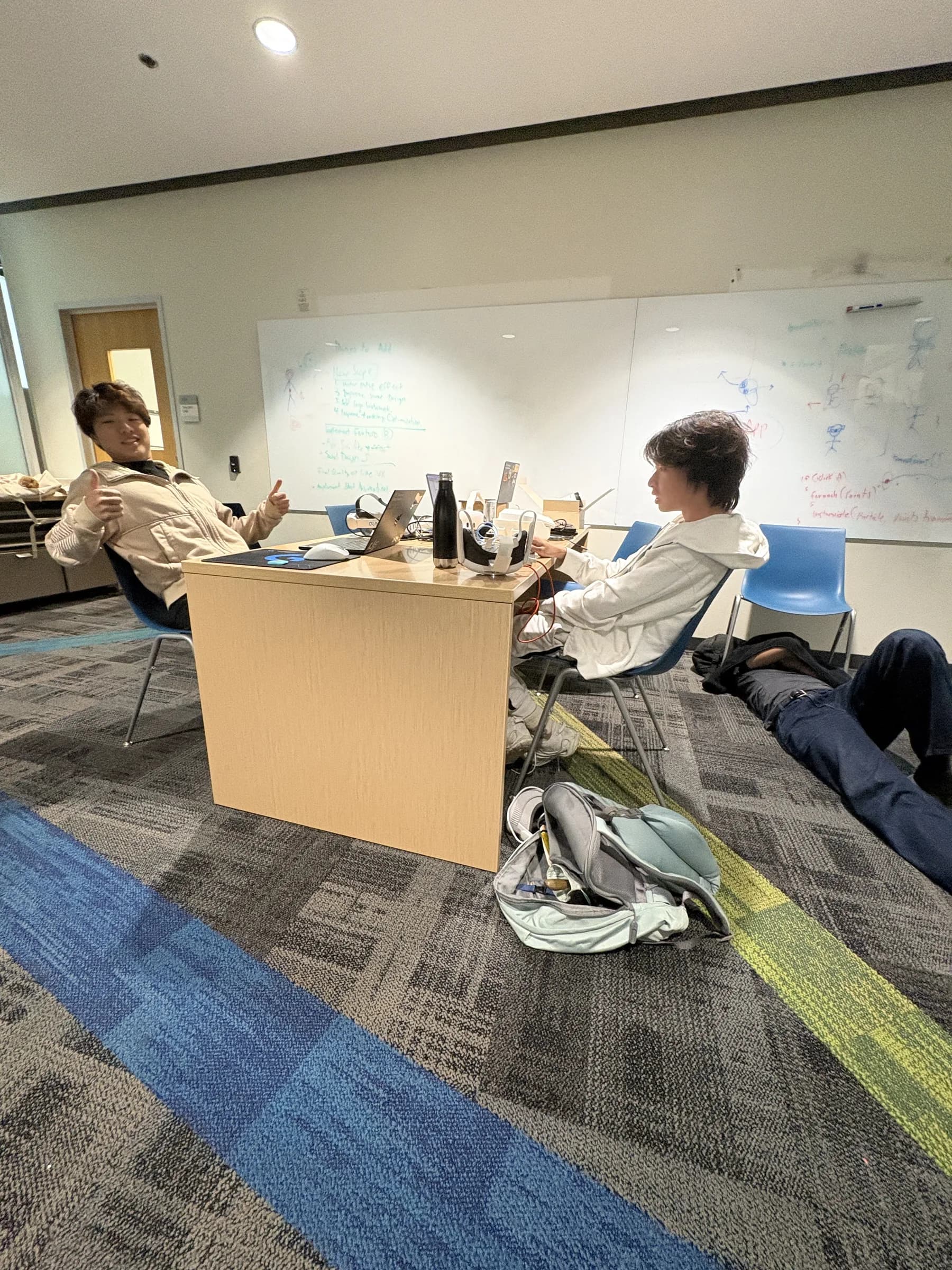 Hackathon photo: teammates slumped in chairs and on the floor around a table in a whiteboard-covered room.