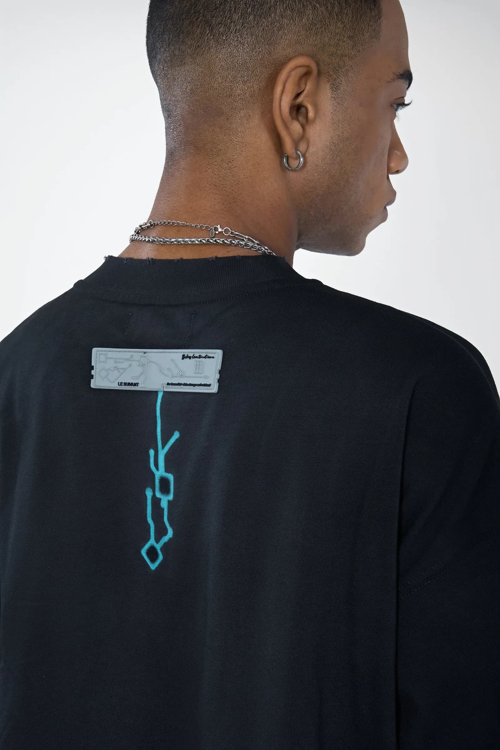 Close-up of the Birth tee back: a rubberised grey RAM tag with a cyan motherboard trace running down the spine