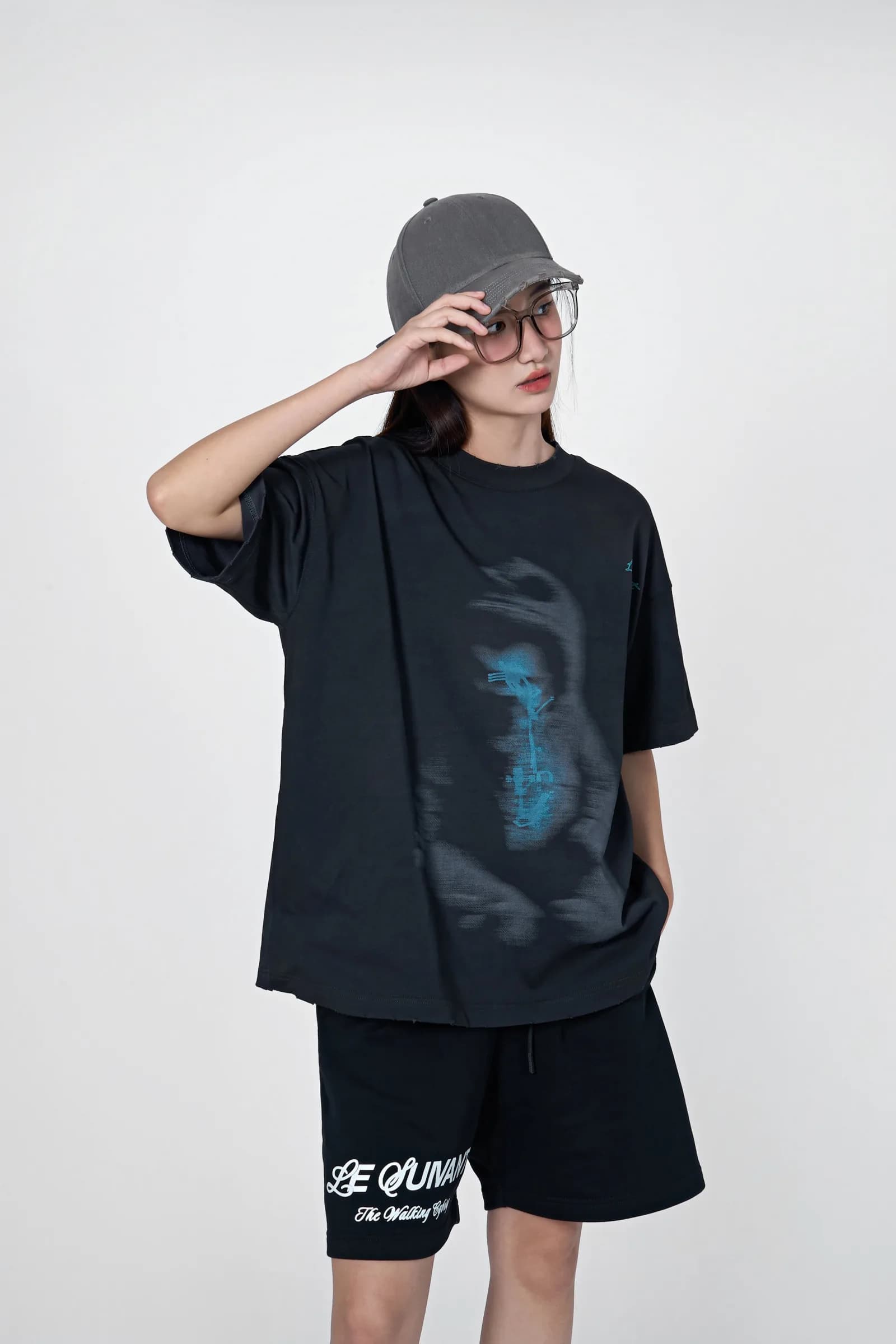 Model in a grey cap and glasses wearing the Birth tee with black Cyborg Classic shorts