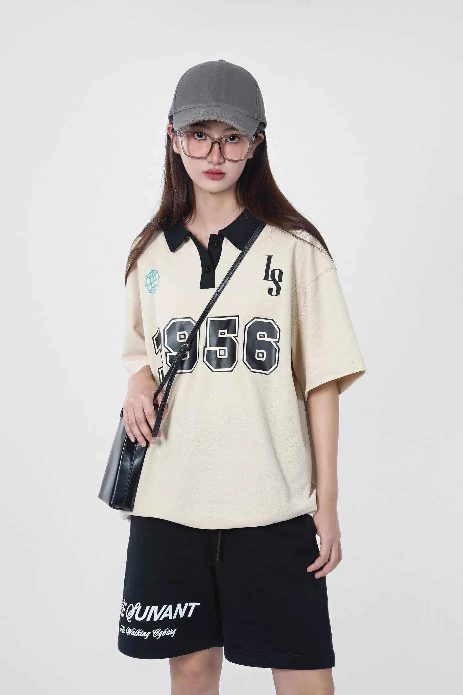 Model in the blanched-almond Butterfly Effect mesh polo with 1956 numerals, black shorts and a black tote