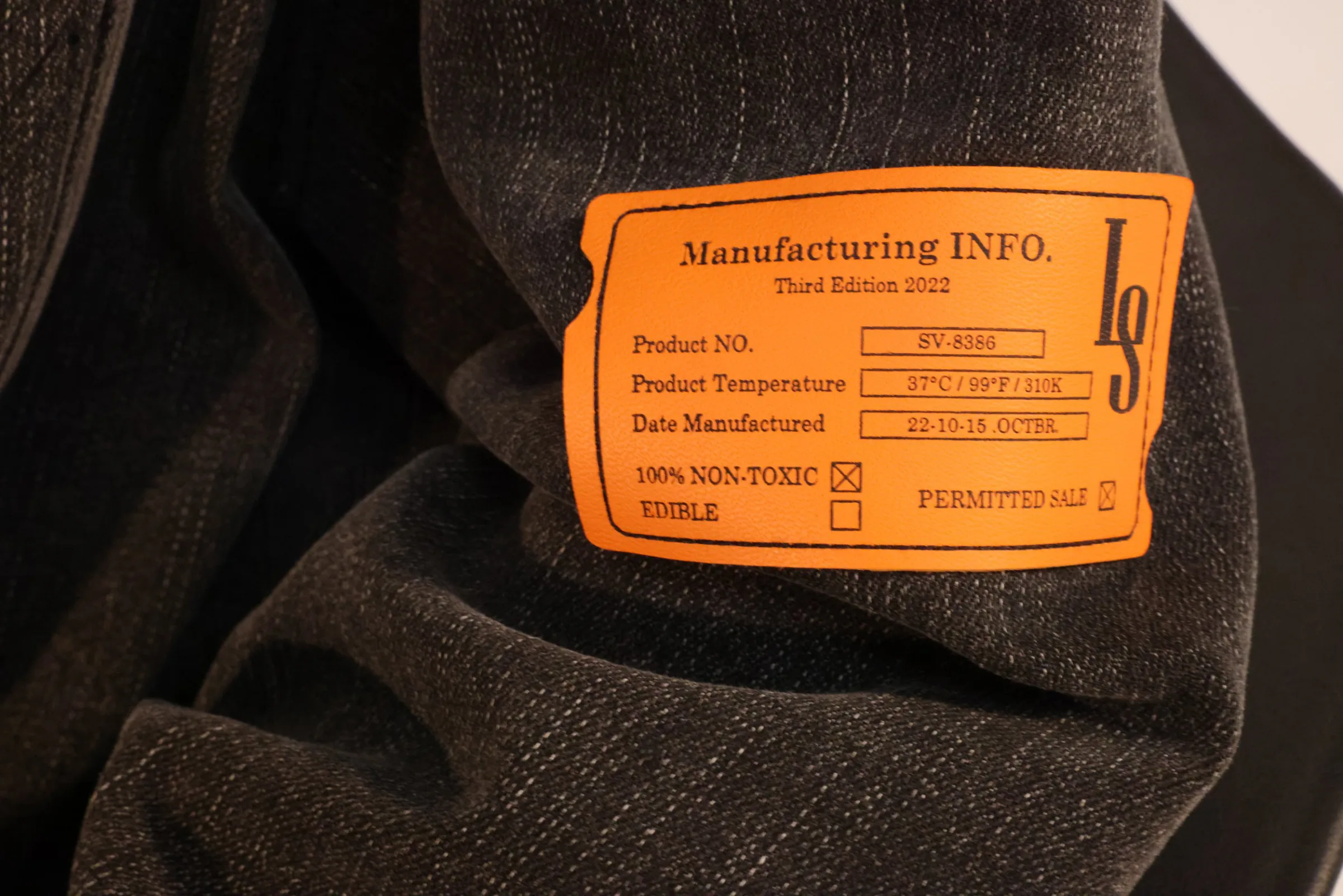Close-up of the orange “Manufacturing INFO.” label stitched onto the charcoal denim hoodie