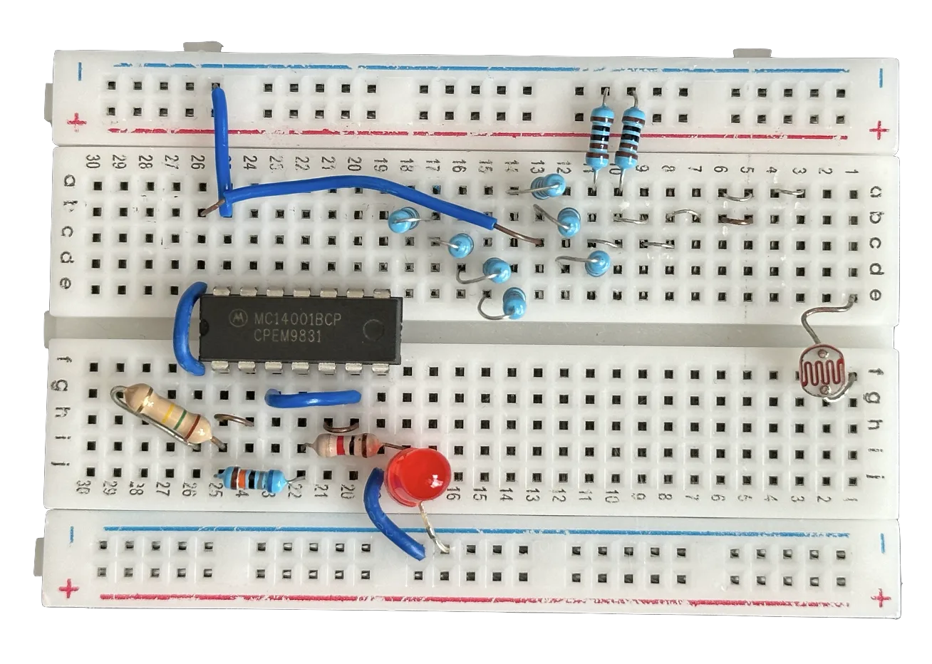 Top-down cut-out of the finished breadboard circuit: an MC14001BCP quad NOR-gate chip, blue and beige resistors, a red LED and a light-dependent resistor